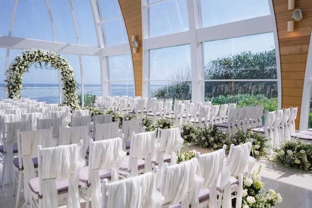 Wedding ceremony set up with rows of white chairs decorated with white ribbons