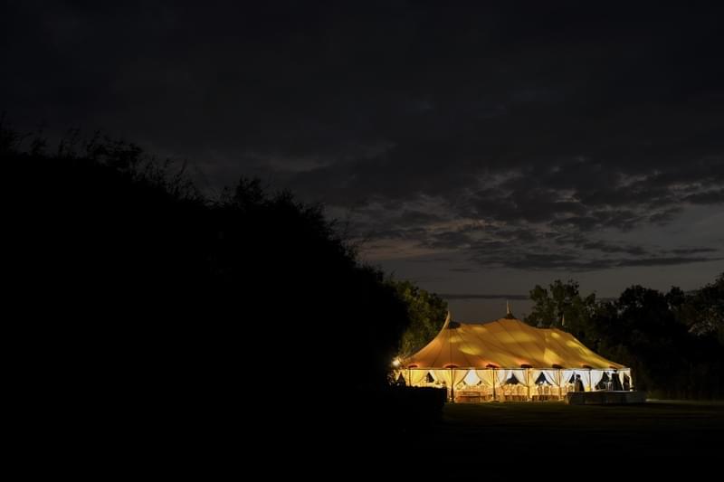  Evening view of an illuminated marquee at Alila Villas Uluwatu, glowing warmly against the night sky and surrounded by lush greenery 