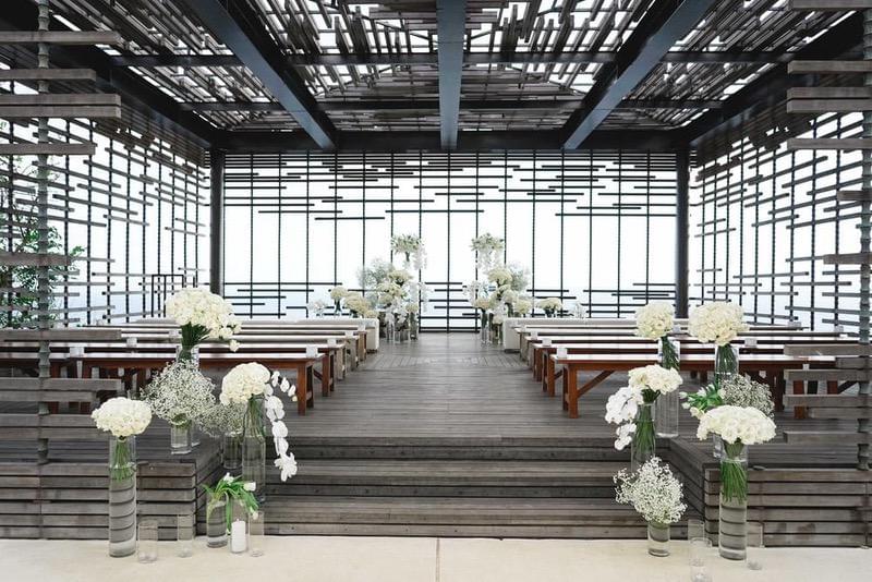  Elegant wedding ceremony setup inside the cabana at Alila Villas Uluwatu, featuring wooden benches, modern architectural details, and white floral arrangements. 