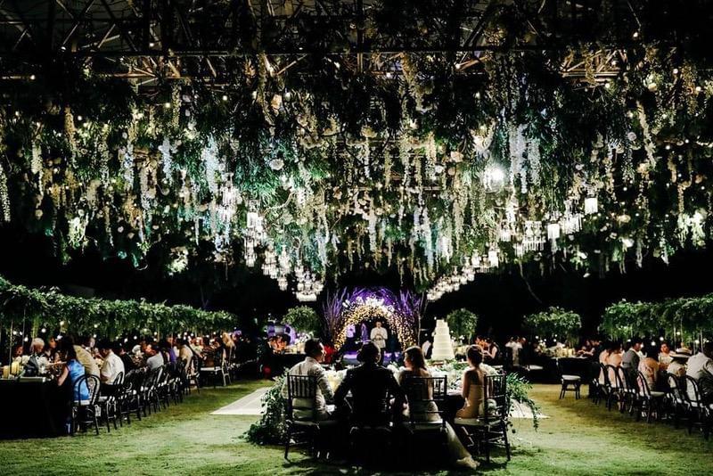  Grand outdoor wedding reception under a marquee at Alila Villas Uluwatu, featuring cascading greenery, hanging lanterns, and long banquet tables filled with elegant place settings and floral arrangements 