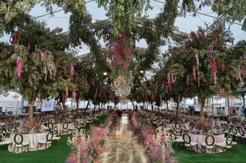  Luxurious wedding reception setup at The Apurva Kempinski, featuring a grand marquee with chandeliers and lush hanging floral arrangements over elegantly arranged tables. 