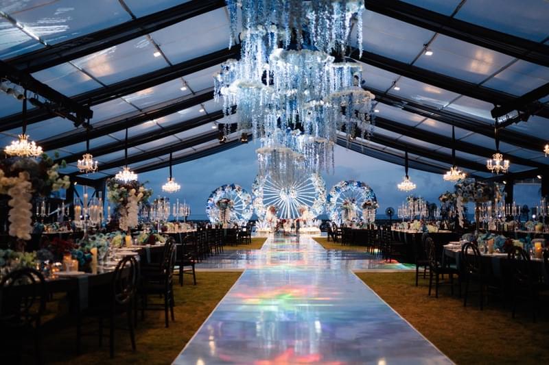  Elegant wedding reception setup on the front lawn at The Apurva Kempinski, featuring a grand tent with chandeliers, colorful lighting, and luxurious decor. 