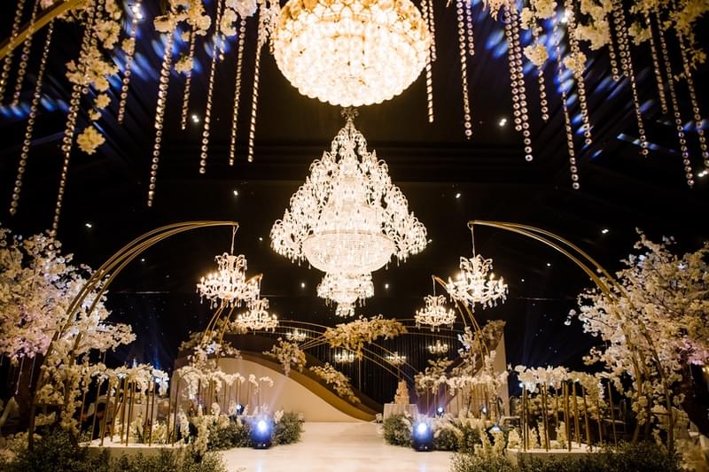  Luxurious wedding reception at The Apurva Kempinski's Candi Ballroom, featuring dramatic chandeliers, floral arrangements, and a grand setup under ambient lighting. 