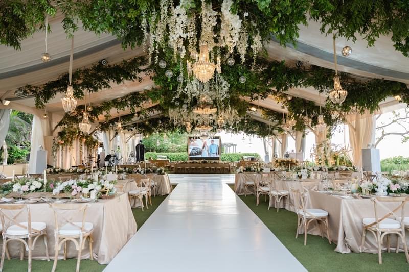  uxurious marquee reception setup on Ayana’s Middle Lawn featuring greenery, crystal chandeliers, cascading floral decor, and elegantly set tables. 