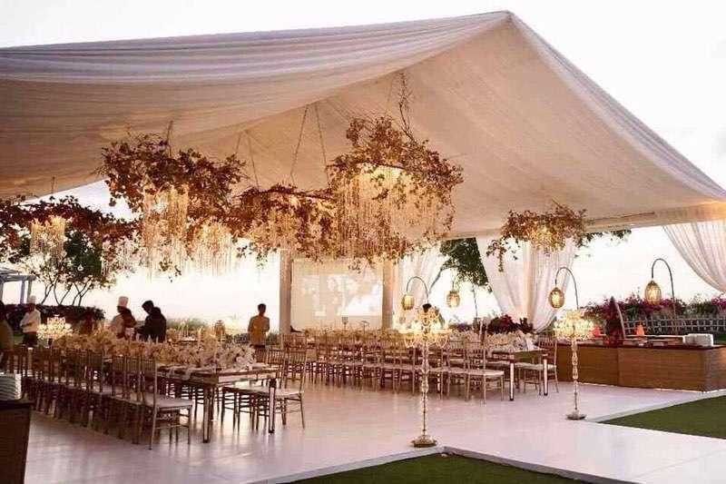  Evening marquee reception with cascading floral chandeliers, warm hanging lanterns, and long banquet tables under a draped canopy. 