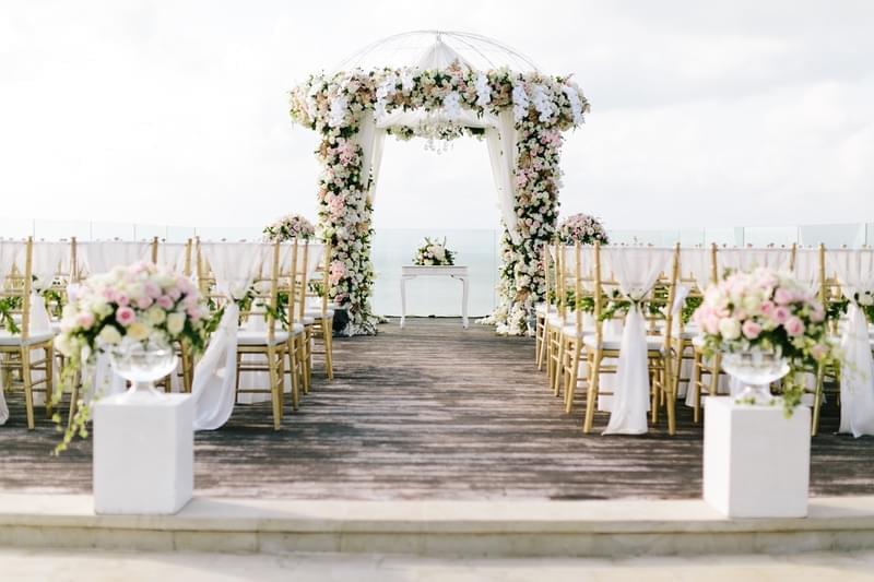 Beautiful wedding setup on the Ayana Villa clifftop deck with a floral arch and elegant gold chairs overlooking the ocean