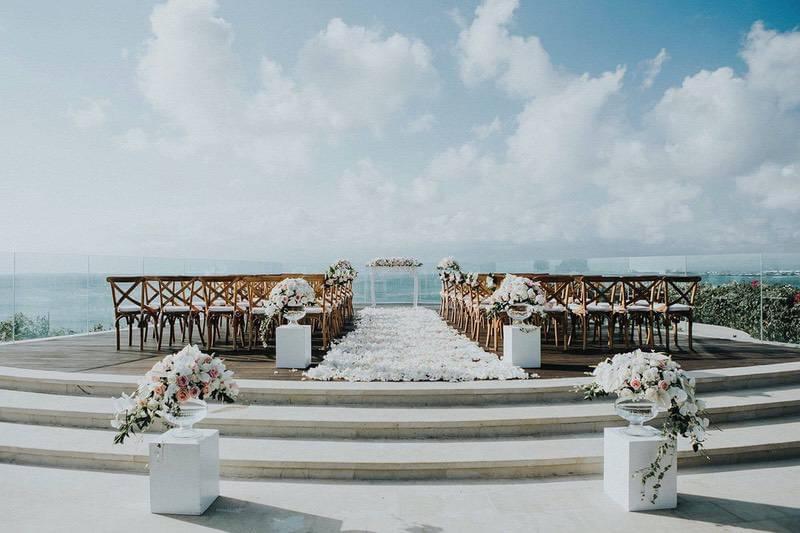 Charming wedding ceremony setup on Ayana Villa's clifftop deck featuring wooden chairs, floral arrangements, and an ocean view backdrop