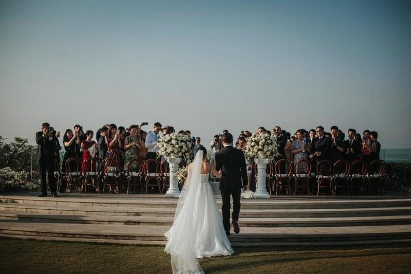 Father walking the bride down the aisle towards the wedding ceremony at Ayana Villa, surrounded by guests and beautiful floral arrangements