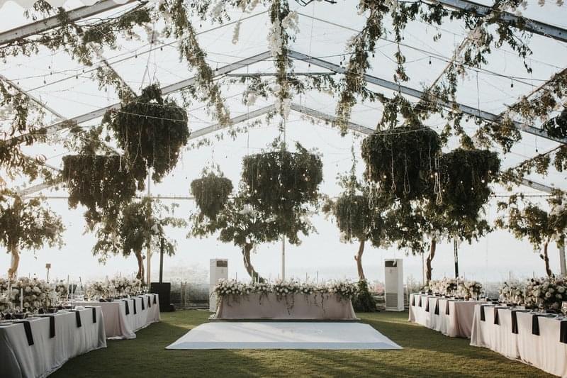 Wedding reception setup under a clear marquee at Ayana Villa, featuring suspended greenery, floral centerpieces, and an elegant dining arrangement