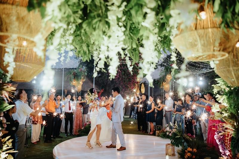 Bride and groom dancing under lush greenery and twinkling lights at their Ayana Villa wedding, surrounded by guests holding sparklers