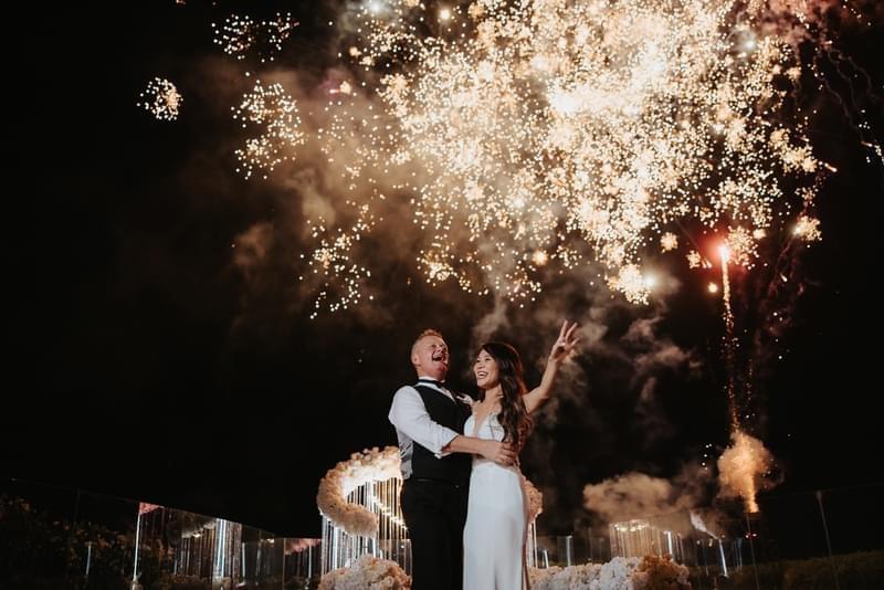 Newlyweds celebrating under a dazzling fireworks display, capturing a magical and joyful moment during their wedding at Ayana Villa