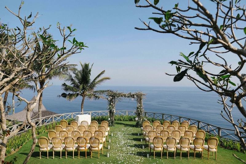  Wedding ceremony setup at Khayangan Estate, featuring wooden chairs and a square floral arch on a clifftop lawn with stunning ocean views 