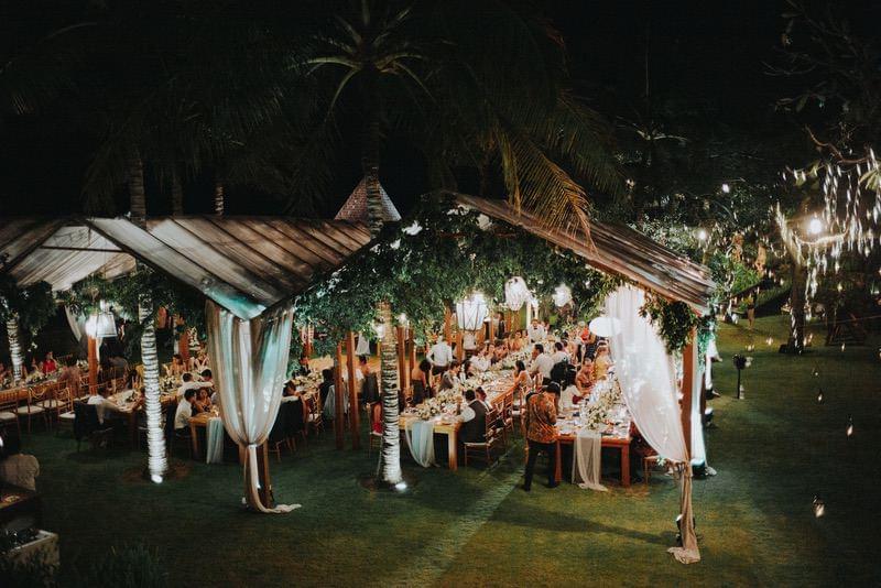  Romantic outdoor wedding reception at Khayangan Estate, featuring long banquet tables, lush greenery decor, soft draped canopies, and intimate lighting under the night sky 