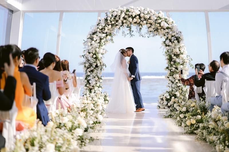  Exquisite wedding ceremony at the Majestic Chapel, featuring a breathtaking floral arch and panoramic ocean views as the couple seals their vows with a kiss. 