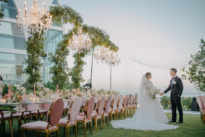  Stunning outdoor bridal table setup with luxurious floral arrangements, chandeliers, and elegant seating, as the bride and groom share a moment at sunset 