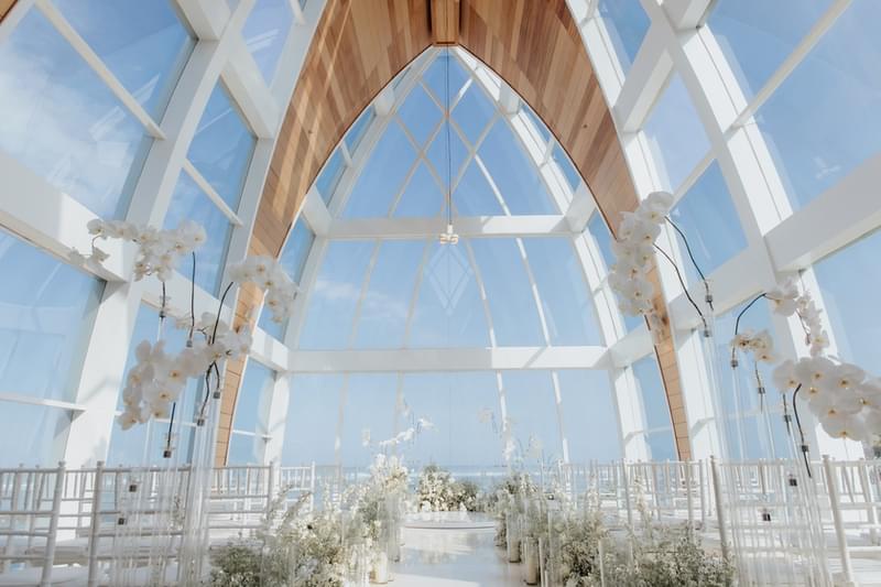  Serene interior of the Majestic Chapel at The Ritz-Carlton Bali, featuring elegant floral arrangements and floor-to-ceiling glass panels showcasing stunning ocean views. 