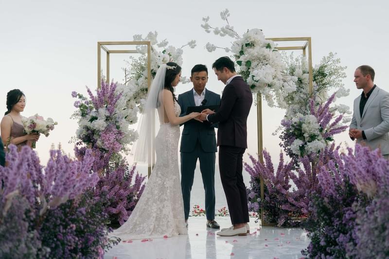  ride and groom exchange vows amidst a romantic floral setup featuring purple and white blooms at The Ungasan 