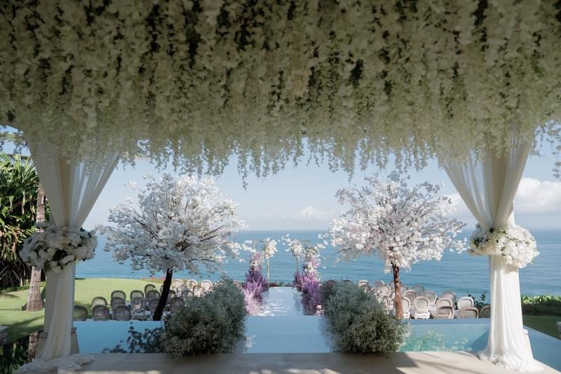  Stunning wedding ceremony setup with cascading floral canopy, blooming trees, and ocean backdrop at The Ungasan 
