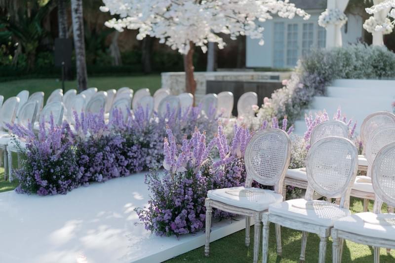  Elegant white chairs and vibrant purple floral arrangements lining the aisle at The Ungasan wedding ceremony setup 