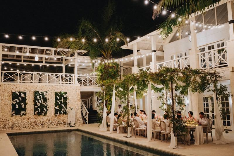 Nighttime wedding reception at Villa Tamarama, with string lights overhead, a beautiful outdoor dining setup by the pool, and guests enjoying an intimate celebration 
