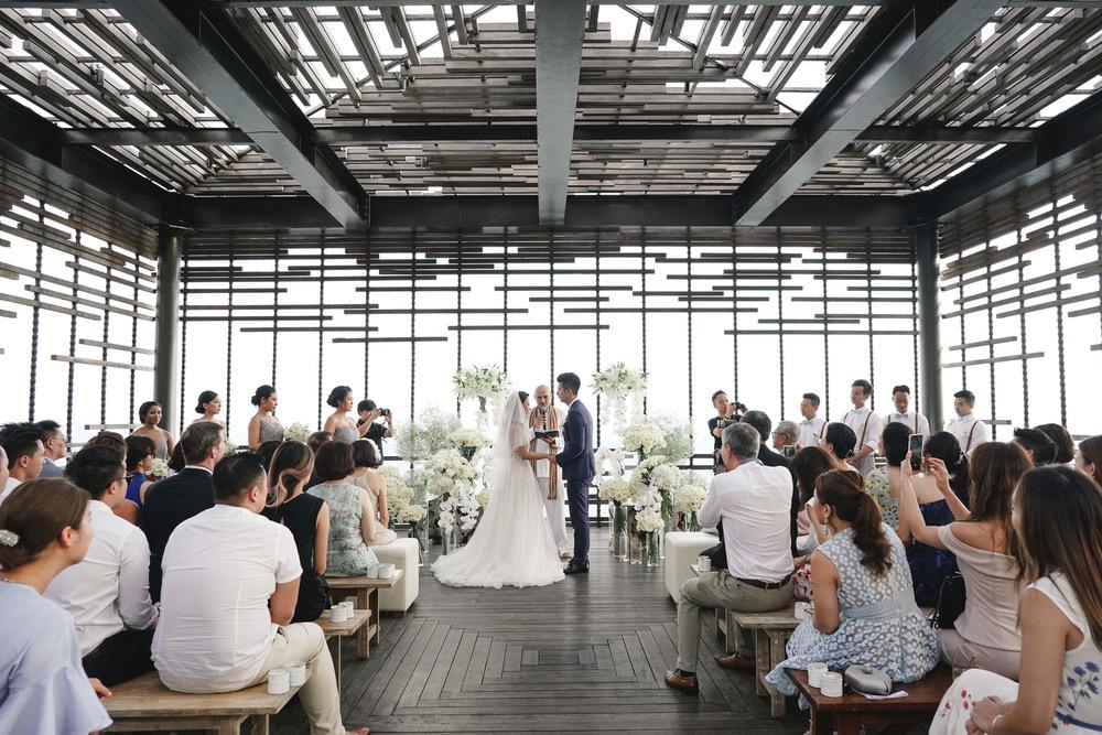 Elegant wedding ceremony at Alila Uluwatu's cliffside cabana, with the couple exchanging vows in a modern open-air structure, surrounded by guests and ocean views