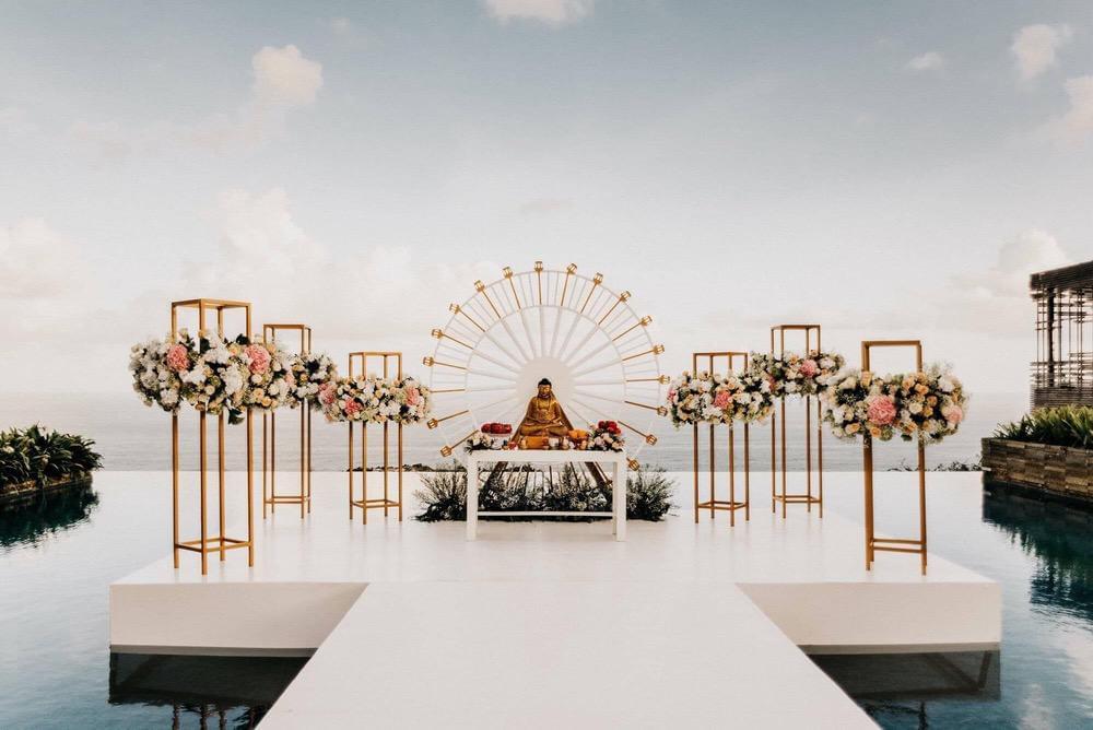 Buddhist wedding ceremony setup on Alila Uluwatu's floating stage, featuring a serene altar with a Buddha statue, elegant floral arrangements, and panoramic ocean views