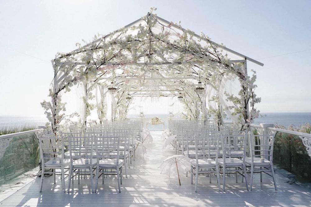 Elegant wedding ceremony setup on Ayana's Sky Platform in Bali, featuring a floral archway, white chairs, delicate parasols, and a stunning ocean view backdrop.