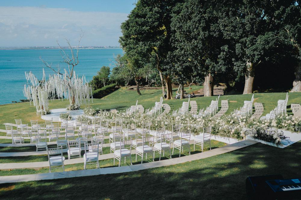 Beautiful outdoor wedding ceremony setup at Ayana's Sky Amphitheatre in Bali, featuring white chairs, floral arrangements, and a stunning ocean view in the background.