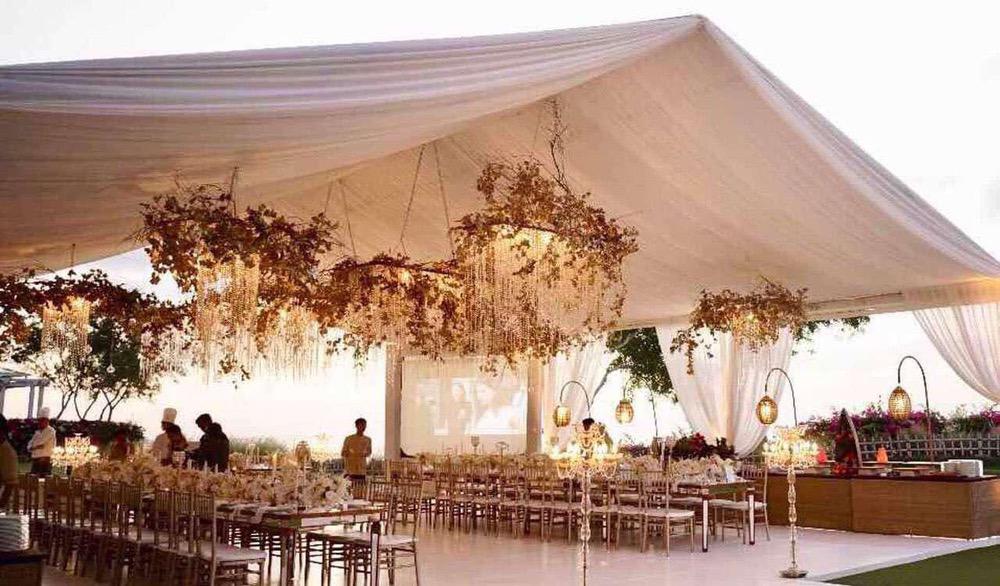 Elegant wedding reception setup under a white marquee at Ayana's Sky Middle Lawn in Bali, featuring floral chandeliers, long dining tables, and warm ambient lighting.