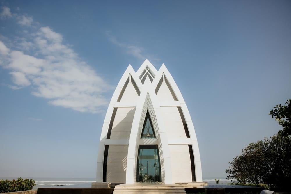 triking exterior of the Majestic Chapel at The Ritz Carlton Bali, featuring modern architectural design with triangular arches and ocean views in the background.