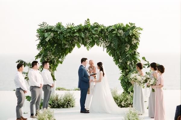 Bride and Groom with bridemaids and groomsmen standing in fron of green flower arch