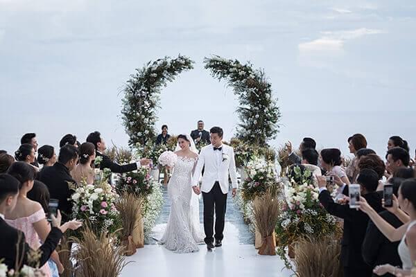 Bride and groom joyfully walking down the aisle after their ceremony at Alila Villas Uluwatu, surrounded by cheering guests and a floral arch in the background