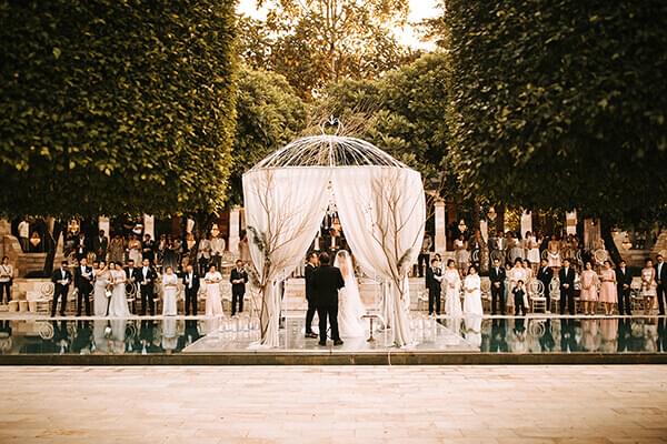 Wedding guests looking on the bride and groom gettingmarried on a floating stage and a white pergola